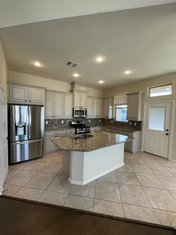 a view of kitchen with stainless steel appliances kitchen island granite countertop dining table chairs and a refrigerator