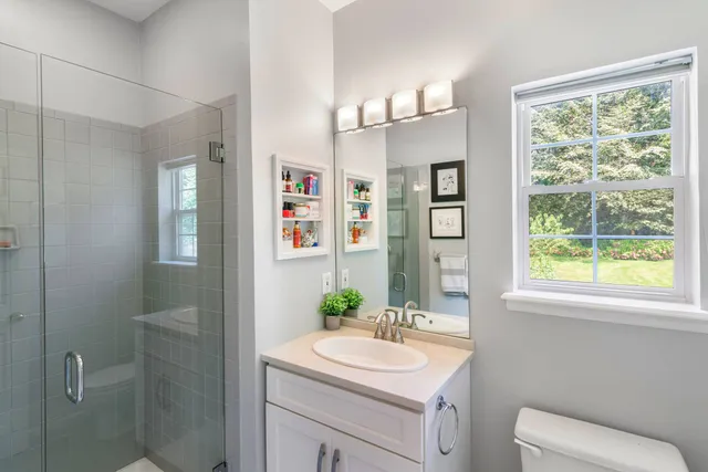 a bathroom with a toilet a sink a mirror a shower and a window