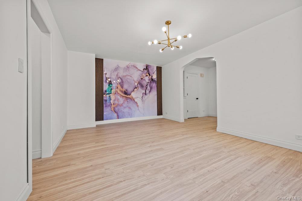 124-16 84th Road, Unit 1D Queens, NY 11415 - Photo 1 of 1 Unfurnished room featuring arched walkways, light wood-type flooring, a chandelier, and baseboards