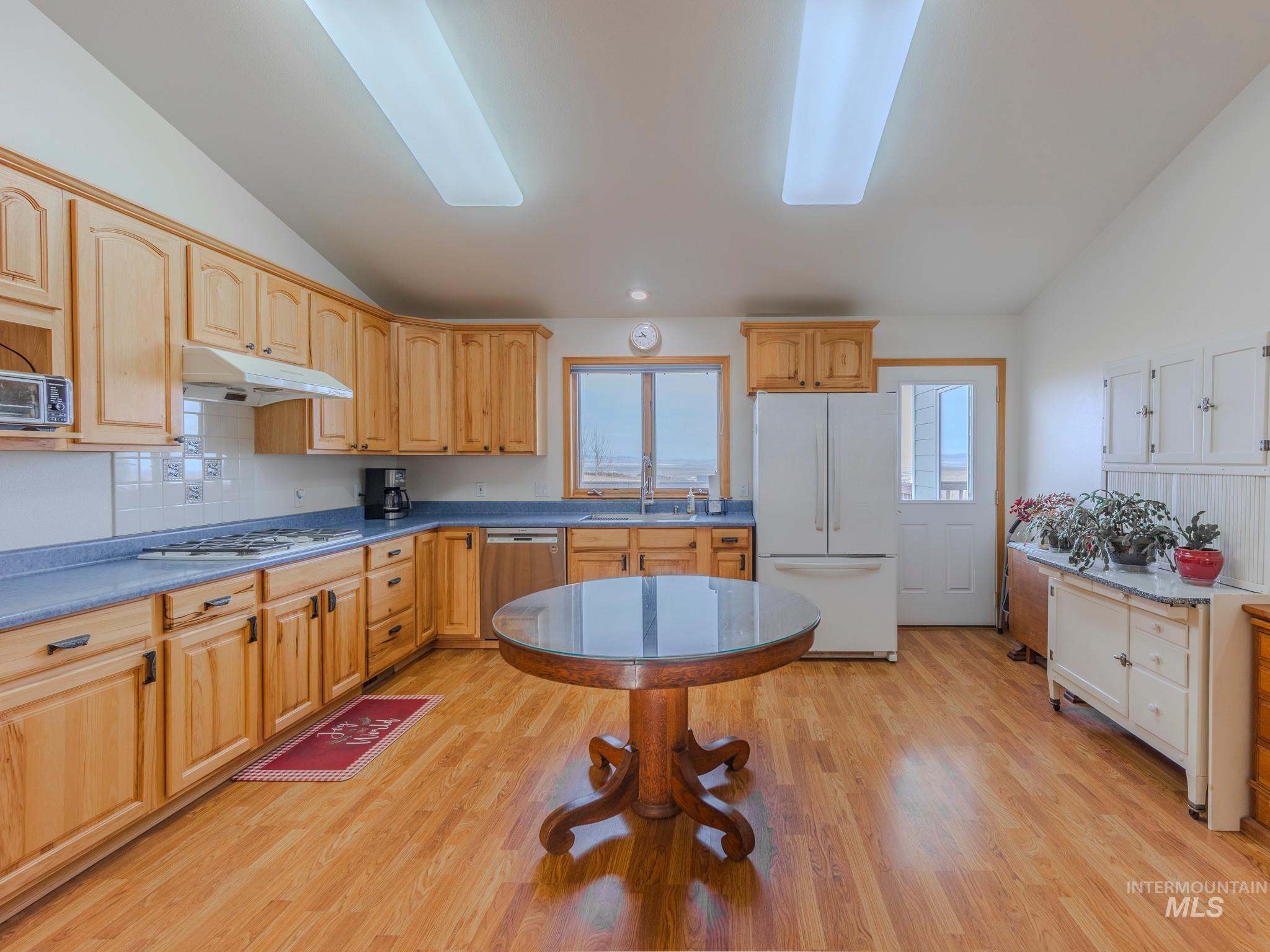 202 Fish Hatchery Road Grangeville, ID 83530 - Photo 10 of 50 Kitchen with vaulted ceiling, white appliances, decorative backsplash, light wood finished floors, and under cabinet range hood