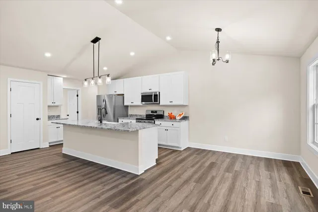 a kitchen with stainless steel appliances granite countertop a sink a stove a refrigerator and white cabinets with wooden floor