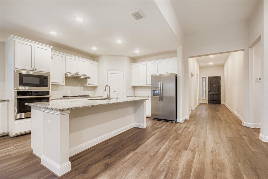 312 Magnolia Drive Oak Point, TX 75068 - Photo 8 of 28 Kitchen featuring tasteful backsplash, stainless steel appliances, white cabinets, light wood finished floors, and a center island with sink