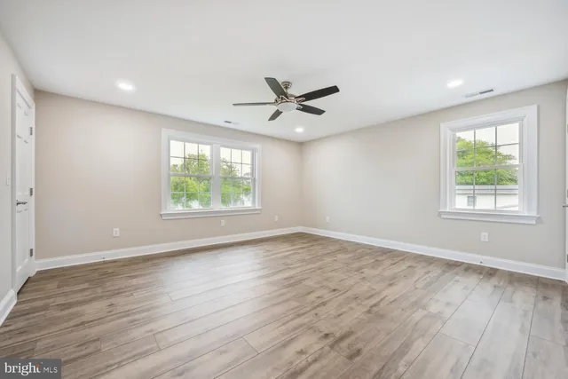 an empty room with wooden floor windows and fan