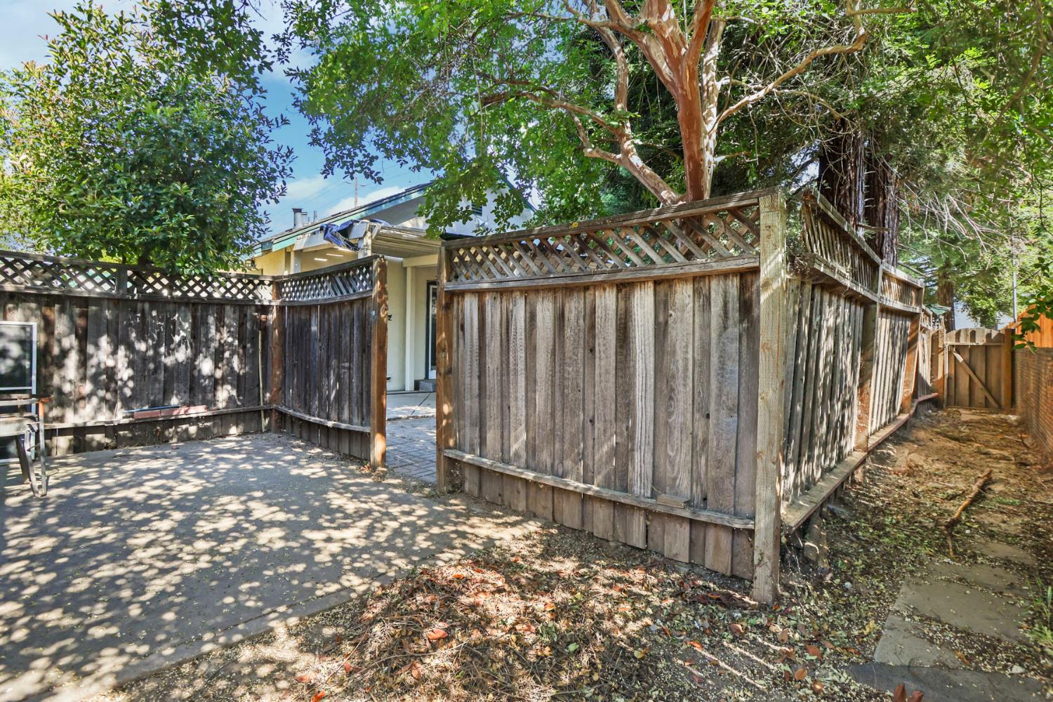 916 Elm Avenue Modesto, CA 95351 - Photo 49 of 52 Fenced side yard and patio area showing privacy fencing, mature shade trees, and access between outdoor spaces.
