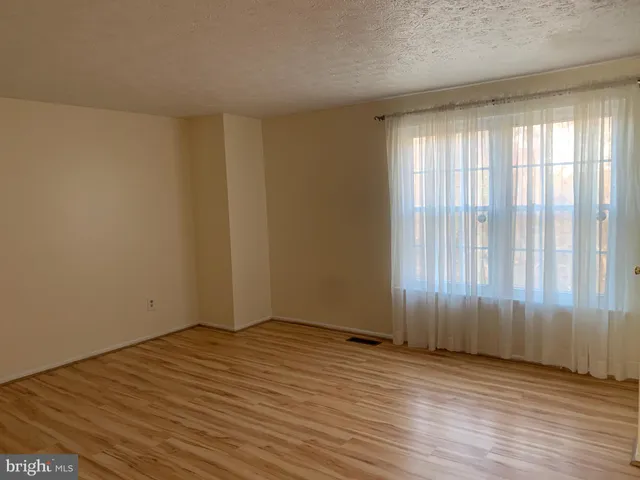 an empty room with wooden floor and windows with curtains