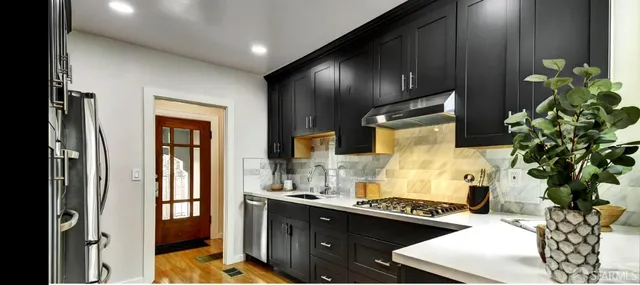 a kitchen with stainless steel appliances granite countertop a refrigerator a sink dishwasher a stove and a dining table with wooden floor