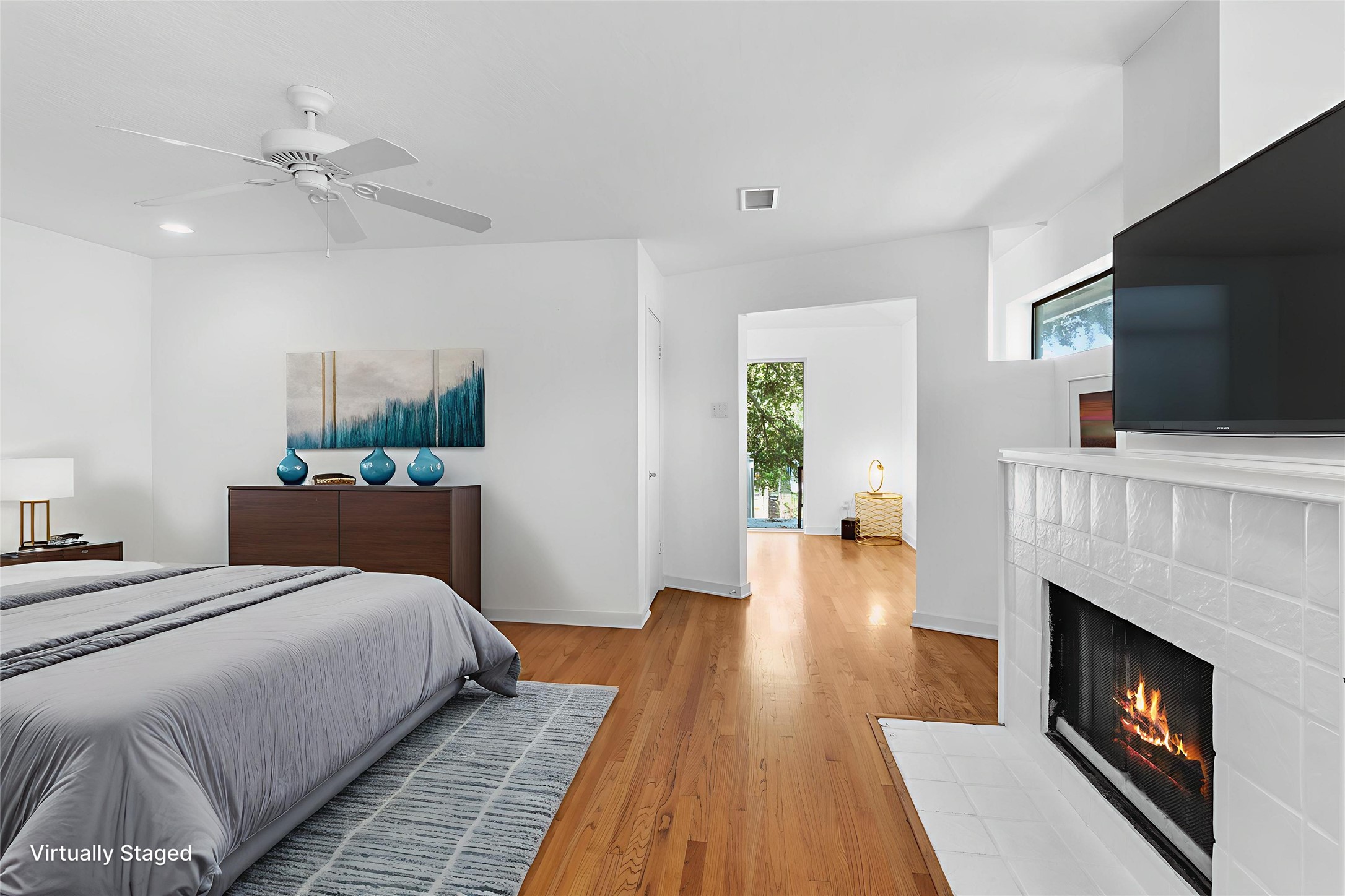 67 Harbor Lane Kemah, TX 77565 - Photo 13 of 47 This inviting primary bedroom features hardwood floors, a cozy fireplace, and abundant natural light. Enjoy a serene atmosphere with neutral tones, minimalist decor, a ceiling fan, and stair access to attic storage. (Staged photo)