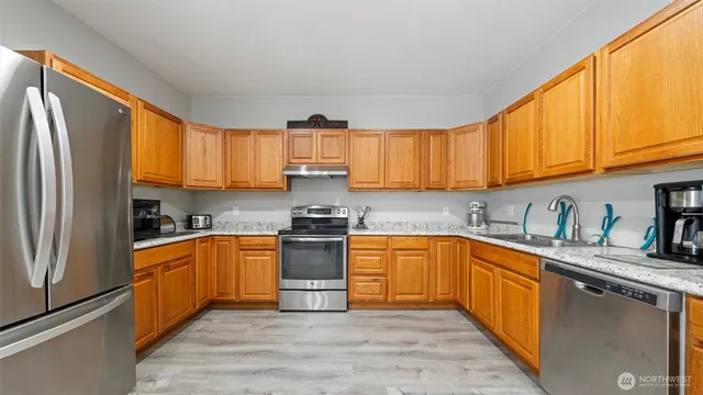 a kitchen with stainless steel appliances granite countertop a stove top oven a sink dishwasher a refrigerator and cabinets with wooden floor