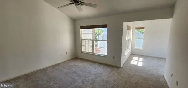 an empty room with chandelier fan and windows