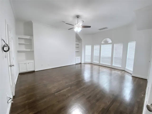 a view of an empty room with wooden floor and a ceiling fan