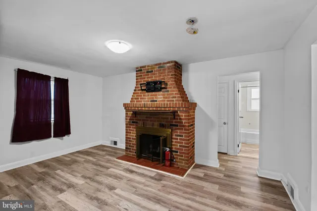 a view of an empty room with wooden floor fireplace and a window