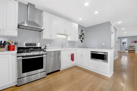 a white kitchen with stainless steel appliances granite countertop a stove a sink and a microwave
