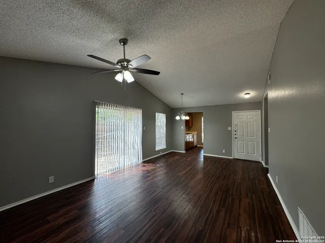 a view of an empty room with wooden floor and a ceiling fan