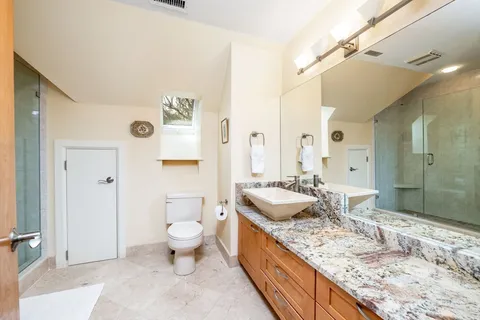 a bathroom with a granite countertop sink a toilet a mirror and shower