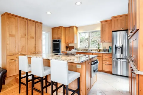 a kitchen with stainless steel appliances granite countertop a stove a refrigerator a kitchen island and chairs in it