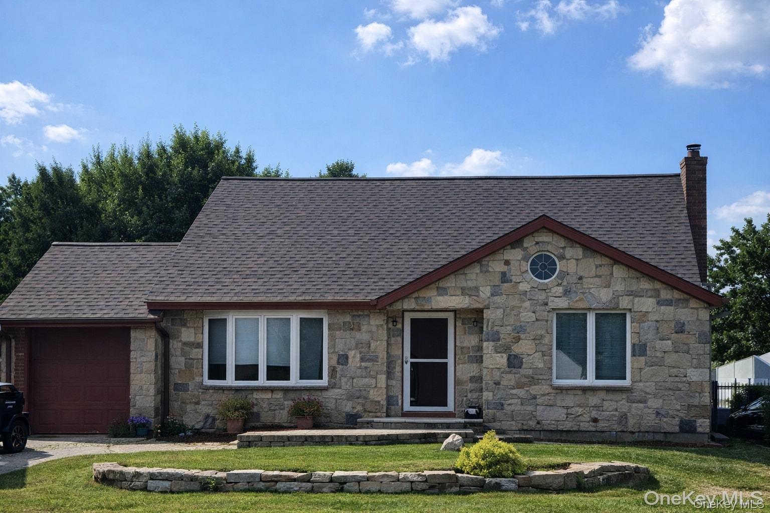 Tudor-style house featuring an attached garage, a chimney, a front yard, and roof with shingles