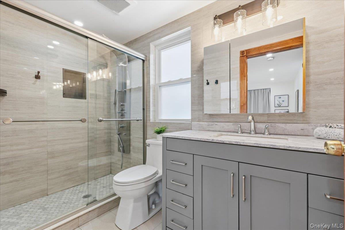 85 Briarcliff Road Westbury, NY 11590 - Photo 14 of 31 Bathroom featuring vanity, a shower stall, tile walls, and light tile patterned floors