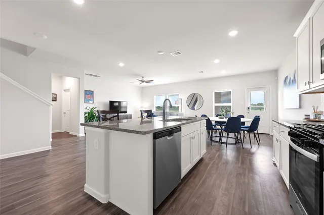 a kitchen with stainless steel appliances granite countertop a stove top oven a sink a dining table and chairs with wooden floor