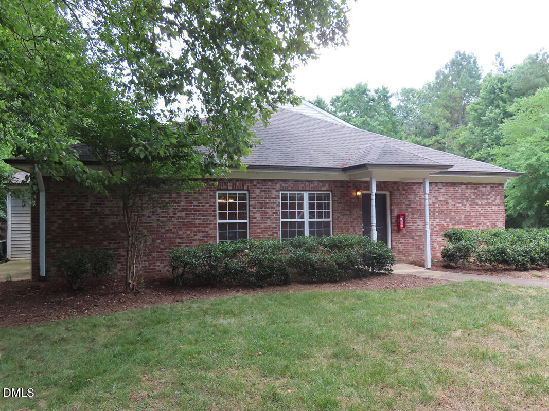 a view of a brick house with a big yard plants and large trees