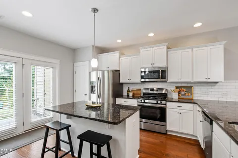 a kitchen with stainless steel appliances granite countertop a stove top oven a refrigerator a sink and dishwasher with a dining table with wooden floor