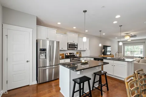 a kitchen with stainless steel appliances granite countertop a refrigerator a stove a sink a dining table and chairs