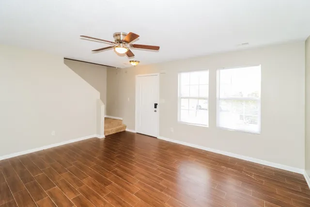 an empty room with wooden floor fan and windows