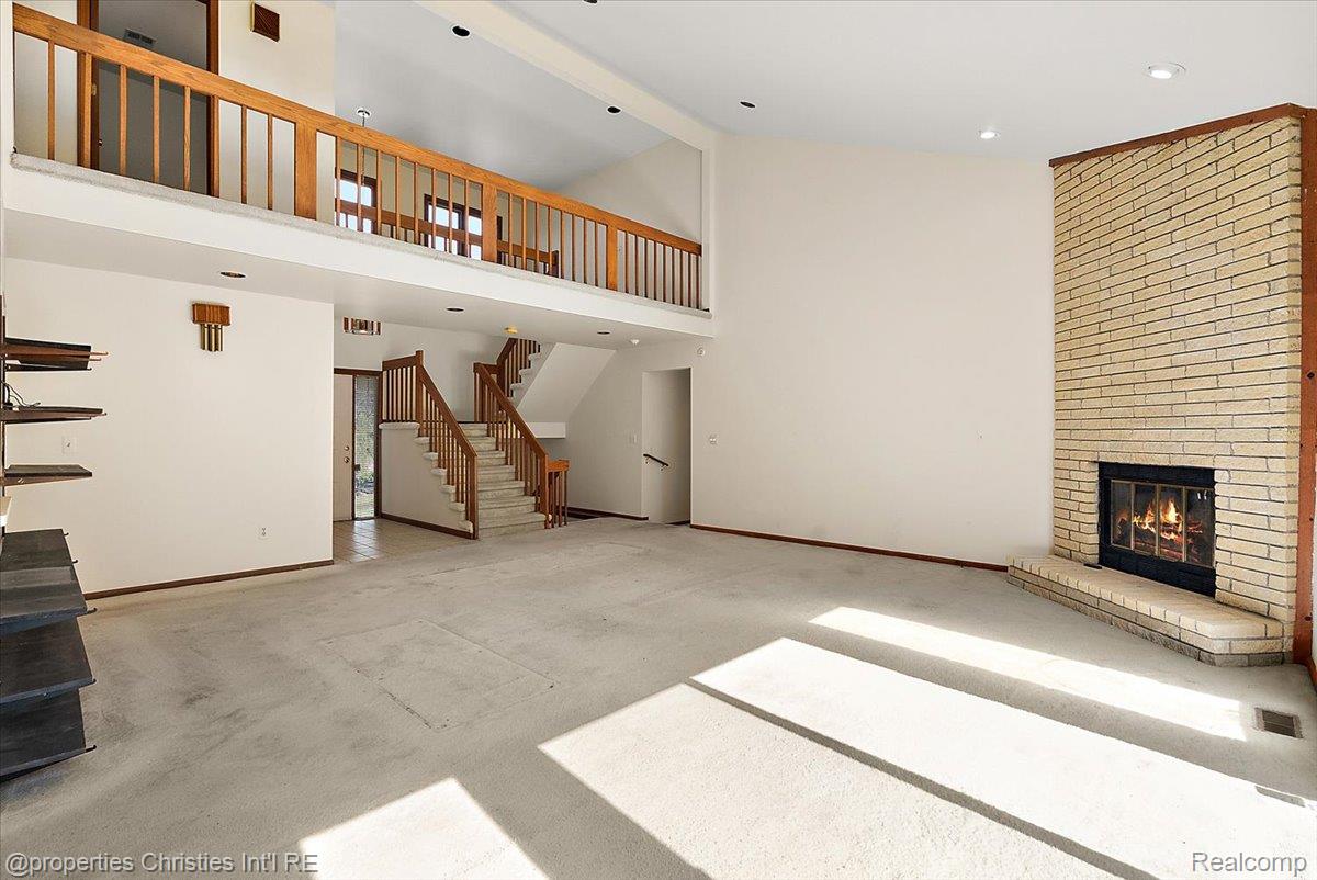 37224 Chesapeake Road Farmington, MI 48335 - Photo 22 of 50 Spacious living area featuring a light brick fireplace with a raised hearth, high ceilings, an upper-level balcony with wood railing, and a staircase with wood banisters