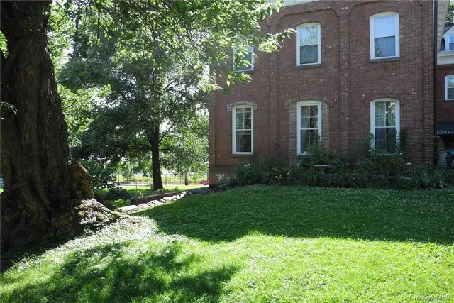 a view of a brick house with a yard and large trees