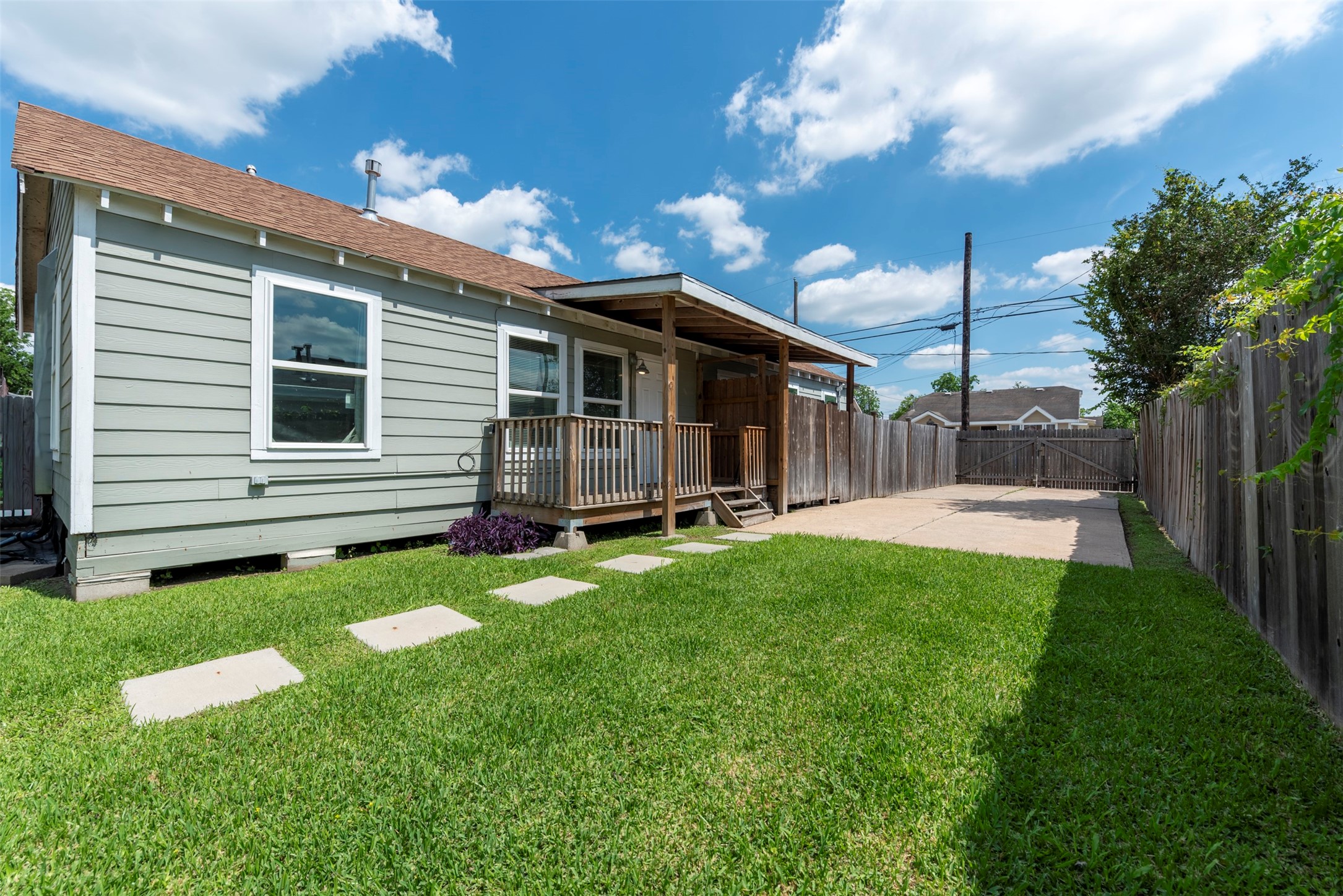 1121 Panama Street Houston, TX 77009 - Photo 2 of 35 Side unit view showcasing sage-green lap siding, white-trimmed oversized windows, covered porch with wood post columns, concrete stepping stone path, and gated driveway access.
