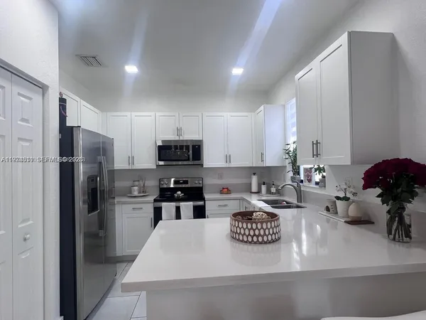 a kitchen with stainless steel appliances kitchen island granite countertop a refrigerator oven a sink a stove and white cabinets