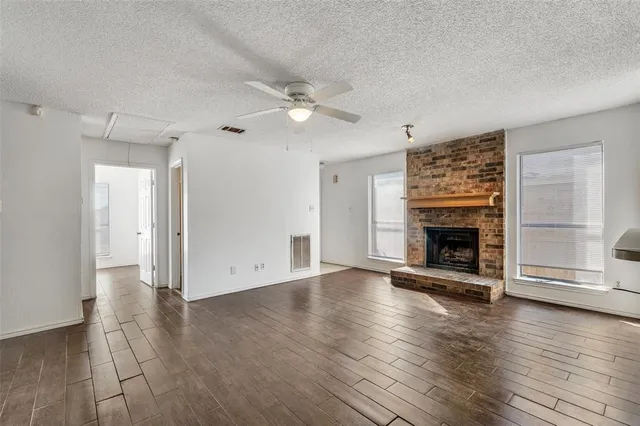 an empty room with wooden floor a ceiling fan a fireplace and windows