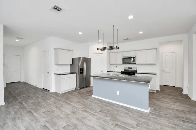 a kitchen with stainless steel appliances kitchen island granite countertop a refrigerator a stove a sink and white cabinets with wooden floor