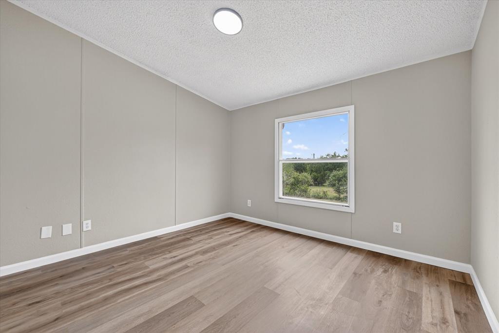 134 Classic Country Court Springtown, TX 76082 - Photo 16 of 35 Interior room featuring wood-finish flooring, light grey walls, white trim, and a prominent window