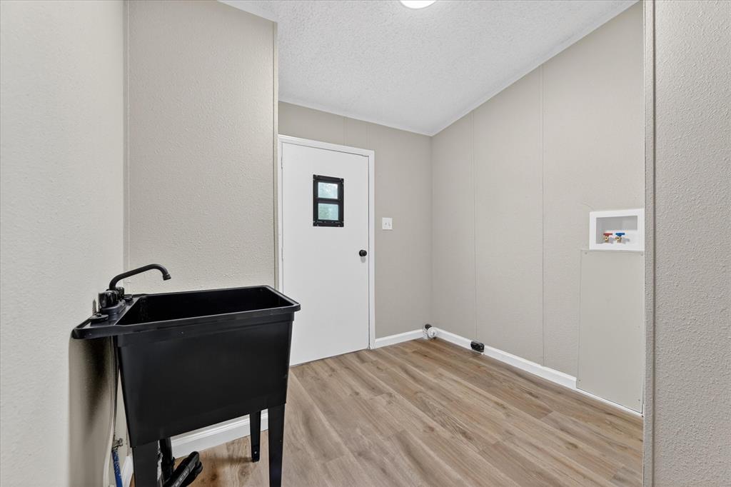 134 Classic Country Court Springtown, TX 76082 - Photo 20 of 35 Utility room featuring wood-finish flooring, light gray wall paneling, a white paneled door with a rectangular window, a black utility sink with a faucet, and washer/dryer hookups