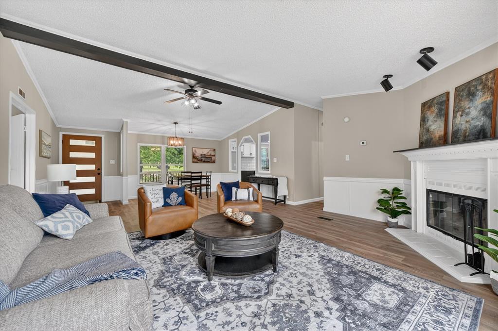 134 Classic Country Court Springtown, TX 76082 - Photo 7 of 35 Spacious living area featuring wood-finish flooring, a white fireplace with an integrated firebox, and a decorative ceiling beam