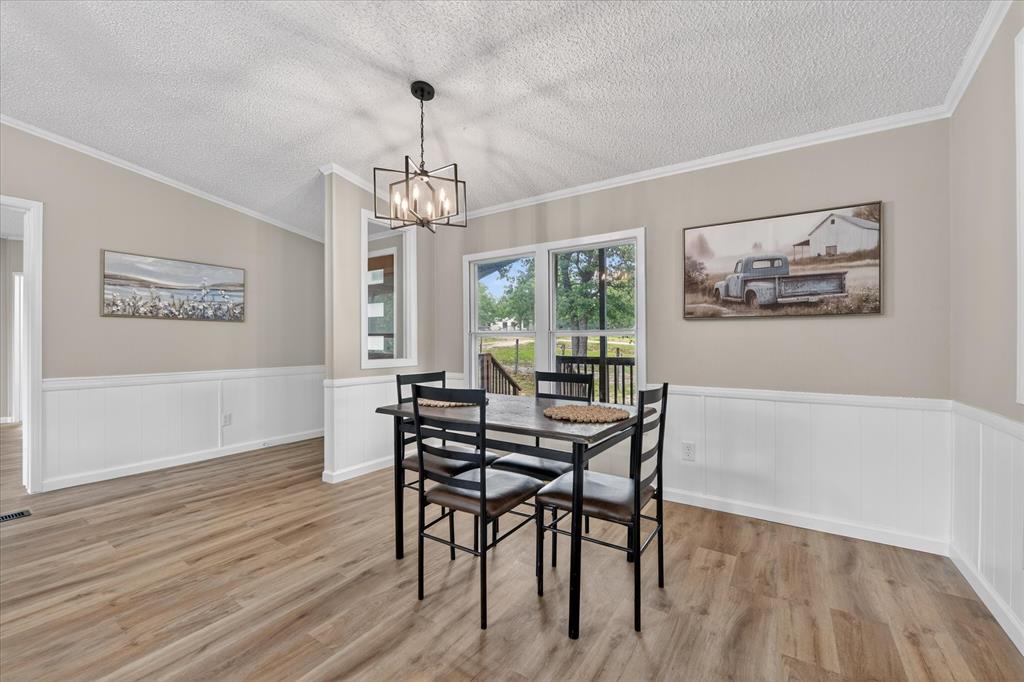 134 Classic Country Court Springtown, TX 76082 - Photo 8 of 35 Dining area featuring wood-finish flooring, white wainscoting, and a modern geometric chandelier