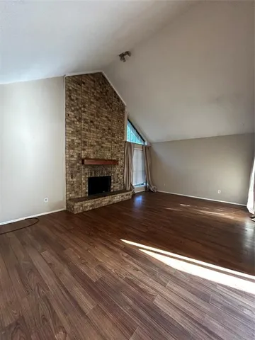 an empty room with wooden floor fireplace and windows