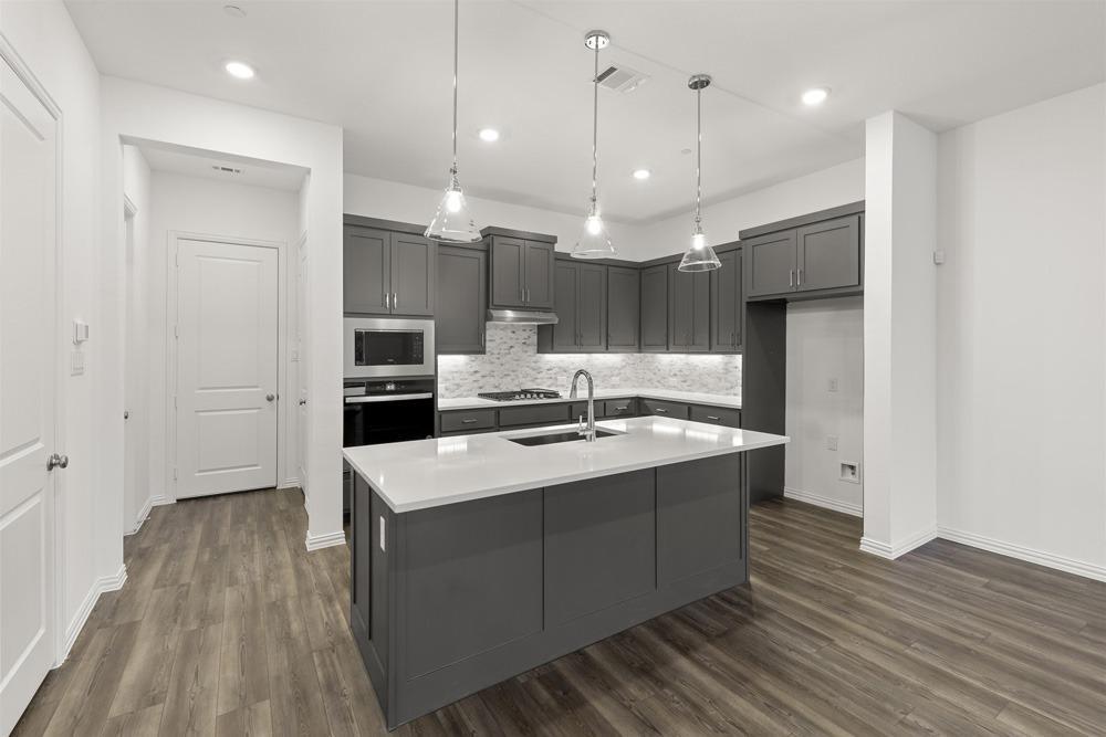 1237 Doris May Drive Allen, TX 75013 - Photo 9 of 19 Modern kitchen featuring a central island with a sink, grey cabinetry, stainless steel appliances, and wood-finish flooring