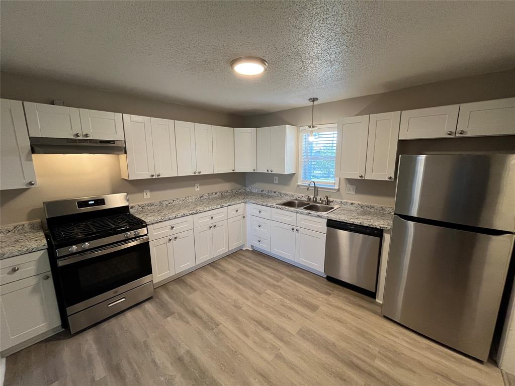 1125 Rancho Drive Mesquite, TX 75149 - Photo 7 of 23 Kitchen featuring appliances with stainless steel finishes, white cabinetry, decorative light fixtures, a textured ceiling, and light stone countertops