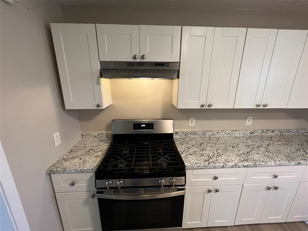 1125 Rancho Drive Mesquite, TX 75149 - Photo 8 of 23 Kitchen with gas range, white cabinets, light stone counters, and under cabinet range hood