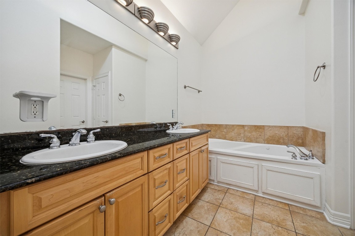 3322 Garden Crest Lane Houston, TX 77018 - Photo 17 of 31 The Primary bathroom features a spacious double vanity with granite countertops, a large mirror, and ample storage in light wood cabinets. It includes a cozy corner bathtub with tile accents and a bright, airy atmosphere.