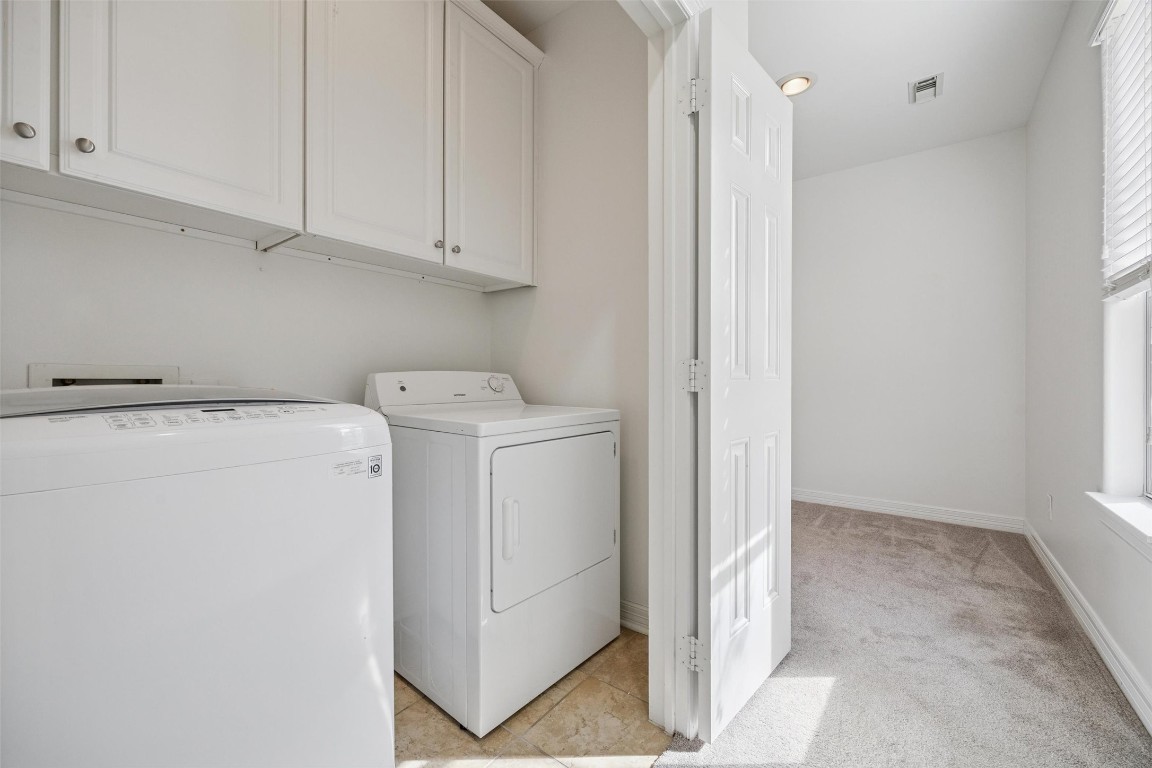 3322 Garden Crest Lane Houston, TX 77018 - Photo 23 of 31 This photo shows a spacious laundry room with a washer and dryer, white cabinets above for storage, and tile flooring. Adjacent is a carpeted area with natural light from a window, offering additional space or utility.