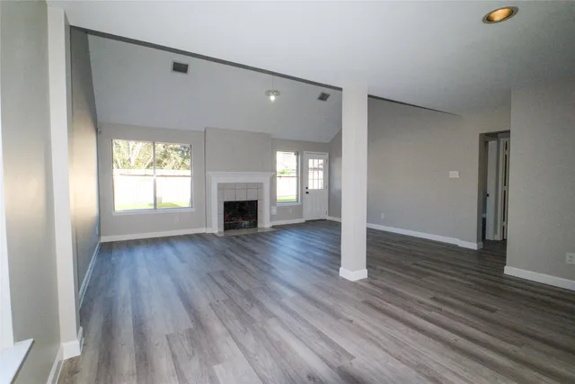 an empty room with wooden floor fireplace and windows