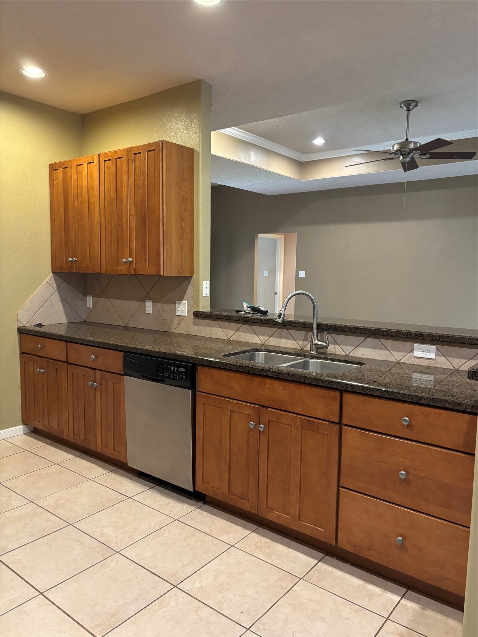 3238 Glenforest Road Montgomery, TX 77356 - Photo 15 of 41 Modern kitchen with ample wooden cabinets and granite countertops. Includes a double sink, stainless steel dishwasher, and tiled backsplash. Open layout with adjacent living space, ceiling fan, and recessed lighting.