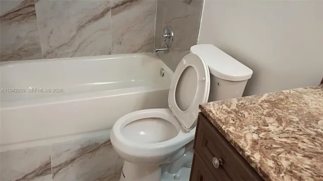 a bathroom with a toilet sink vanity granite and bathtub