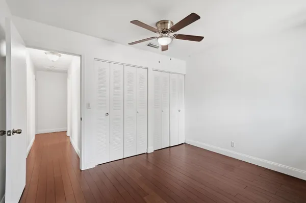 an empty room with wooden floor a ceiling fan and windows
