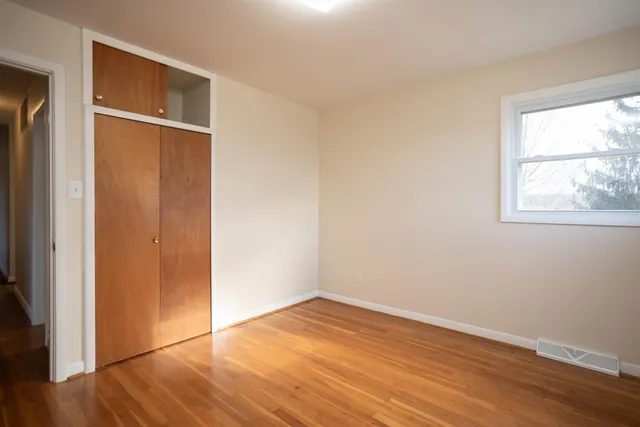 an empty room with wooden floor closet and windows