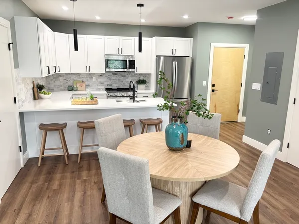 a kitchen with stainless steel appliances granite countertop a dining table chairs refrigerator and microwave