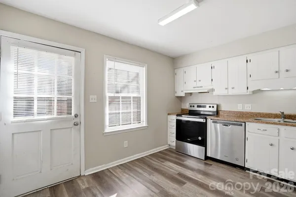 a kitchen with stainless steel appliances granite countertop a stove a sink and white cabinets with wooden floor