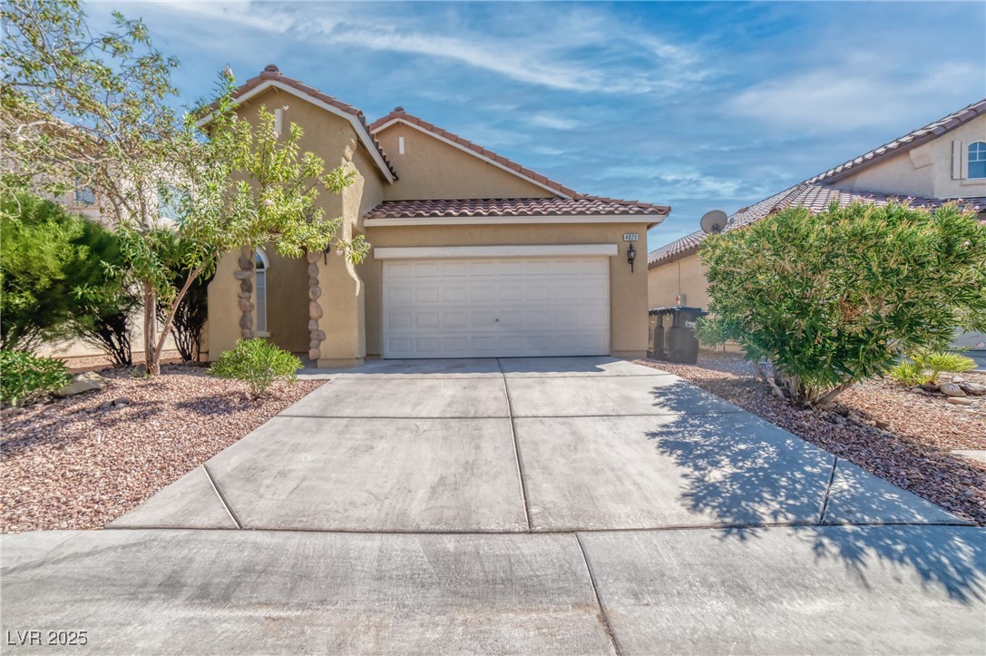 View of front of property with stucco siding, a tiled roof, concrete driveway, and a garage